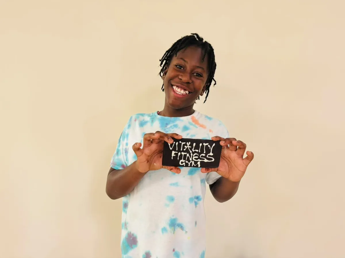 A smiling young supporter holding a handmade Vitality Fitness Gym sign
